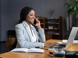 黑人女商人一边在电脑上打字一边打电话.